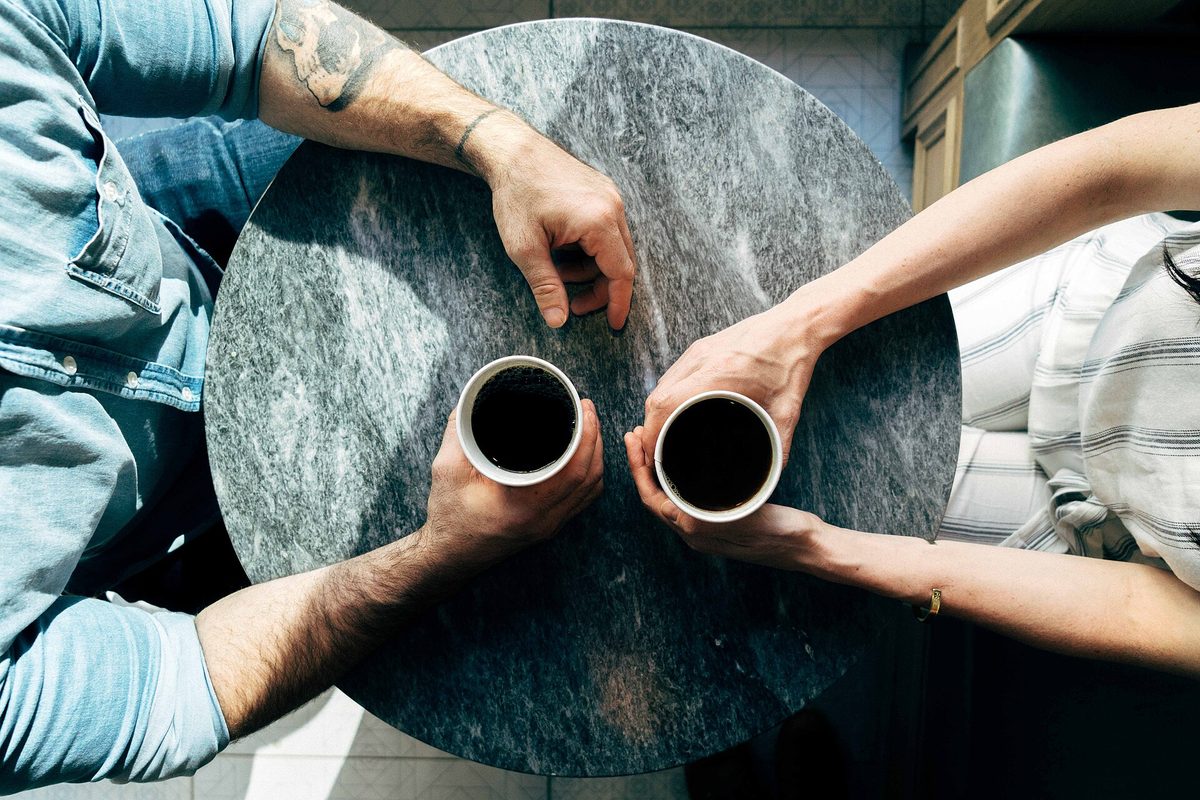 To personer med hver sin kaffekopp ved et marmorbord, sett ovenfra – økonomien er personlig, men felles lån vurderes samlet.