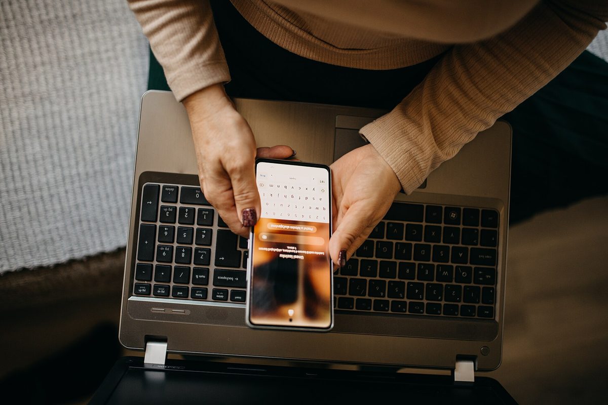 Kvinne logger inn på mobilen med laptopen ved siden av – kredittsperren oppretter du selv på noen få minutter.